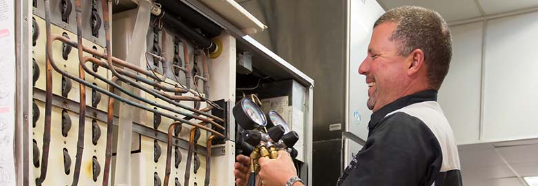 A technician smiles while using diagnostic gauges to inspect and service the internal components of a commercial refrigeration or HVAC unit.